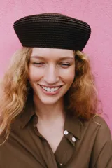 Gorro tipo casquete de diseño circular, confeccionado en tejido de punto trenzado en color marrón oscuro.