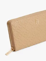 Billetera grande de material sintético color beige, con cierre de cremallera perimetral. Presenta un estampado integral en relieve con el monograma de la marca y un dije metálico con el logo TH en el frente.