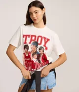 Remera de manga corta color blanco roto con cuello redondo. Presenta un estampado grande en el frente con la palabra "TROY" en letras rojas con textura de puntos blancos, y un collage de cuatro imágenes del actor Zac Efron en su papel de Troy Bolton de High School Musical, rodeado de estrellas rojas.