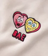 Buzo con capucha de corte boxy, color beige, con bolsillo canguro frontal y estampa bordada de Bob Esponja y Patricio en el pecho. Presenta puños y cintura acanalados, y cordones ajustables en la capucha.