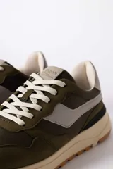 Championes urbanos de diseño técnico, combinando paneles de gamuza y tela en tono verde oliva con detalles en beige y negro. Presentan una suela de plataforma en color crema con base dentada en tono caramelo.