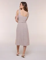 Vestido midi abotonado verde melange, con escote recto, tirantes anchos y falda de calce recto con vuelo sutil. Tiene abotonadura frontal completa con botones estilo carey, cinto textil con hebilla para ajustar la cintura y bolsillos laterales.