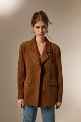 Blazer de gamuza color marrón con cuello solapa, corte holgado y detalle de tachas metálicas en solapas, bolsillos delanteros y puños.