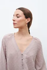 Blusa color beige con textura de lunares en relieve, escote en V y mangas largas con puños elásticos.