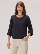 Remera negra de algodón con cuello redondo y mangas tres cuartos acampanadas. Las mangas presentan un diseño con costuras horizontales decorativas en hilo contrastante.