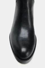 Bota de caña alta estilo hípica, color negro, con detalle de tira con hebilla metálica en la parte superior de la caña. Presenta tacón bajo ancho y punta redonda.