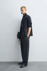 Pantalón negro de corte relajado con cintura elástica ajustable y pliegues en la parte delantera. Presenta bolsillos laterales y bolsillos traseros de parche.