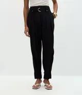 Pantalón de sastrería corte carrot, color negro, con pliegues delanteros, cintura alta y cinturón desmontable con hebilla metálica. Presenta un diseño holgado en las caderas que se estrecha hacia el ruedo con dobladillo estructurado.