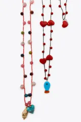 Pack de tres collares de cordones trenzados en tonos rojo y negro, adornados con cuentas de diferentes colores y dijes colgantes: corazones rojos, un dije azul turquesa con forma de pez, un dije azul verdoso con forma de corazón y un dije dorado con textura de concha.