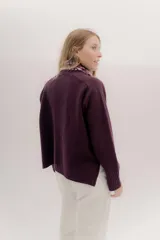 Polera tejida en lambswool color beige, con cuello alto y diseño de intarsia en tonos marrones y grises. Presenta botones forrados en el cuello para modular la apertura.