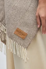 Ruana de lana sin teñir en tono marrón jaspeado, con diseño envolvente y terminaciones de flecos en color crudo.