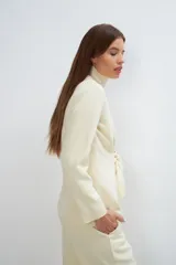 Chaqueta corta color beige, entallada, con escote en V, manga larga y bolsillos escondidos. Cierre frontal con lazo fijo. Confeccionada en lana fina sin teñir. Diseño exclusivo de Don Baez.