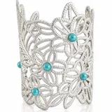 Brazalete ancho de metal plateado con diseño calado de flores entrelazadas y detalles de piedras turquesas redondas en el centro de algunas flores.