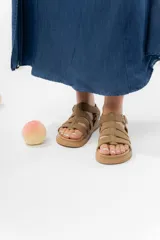 Sandalia estilo gladiadora color suela, confeccionada en material gamuzado sintético. Presenta múltiples tiras anchas que sujetan el pie, ajuste lateral con hebilla metálica y suela plana antideslizante.
