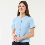 Camiseta de punto celeste con cuello redondo, mangas cortas y cierre frontal de botones, adornada con volantes en la botonadura, los puños y el dobladillo.