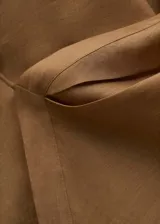 Camisa de ramio color tostado con cuello camisero, manga larga con puños abotonados y cierre frontal parcial con tres botones. Presenta un diseño cruzado en el frente y bajo asimétrico.