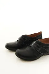 Zapato de cuero negro con cierre de velcro ancho y costuras pespunteadas a contratono.