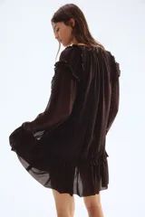 Vestido corto negro de manga larga con escote redondo. Presenta secciones drapeadas y fruncidas en el torso y el bajo, con ribetes de volados a lo largo de los bordes del drapeado y en los puños.