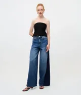 Pantalón wide leg de denim azul con cintura mediana y recorte lateral en tono más oscuro que alarga la silueta. Cuenta con trabillas, cierre frontal tradicional y bolsillos.