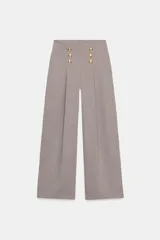 Pantalón de tiro alto con pierna ancha, confeccionado en sarga color tostado. Presenta detalle de doble hilera de botones metálicos dorados en el frente y pinzas verticales.