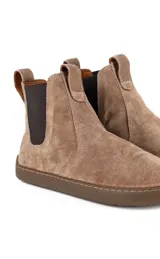 Botas estilo chelsea barefoot de gamuza color arena, con elásticos laterales en color marrón oscuro, suela plana y flexible, y tirador trasero.