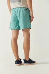 Short de baño liso para hombre, con cintura elástica y cordón ajustable. Cuenta con dos bolsillos laterales, un bolsillo trasero y logo bordado en la parte inferior.