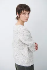 Buzo de tejido de punto con cuello redondo, mangas largas y textura jaspeada en tonos neutros.