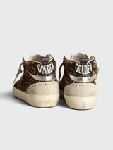 Zapatillas Golden Goose modelo Mid Star con diseño de caña media, confeccionadas en piel con estampado de leopardo y detalles en gamuza beige. Presentan una estrella lateral en color negro, cordones en tono neutro y suela con efecto desgastado.