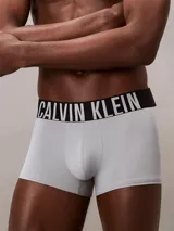 Pack de tres bóxers tipo trunk de Calvin Klein, confeccionados en microfibra elástica. Incluye un par negro, uno gris claro y uno verde brillante, todos con cinturilla elástica negra con el logo de Calvin Klein en contraste (blanco o verde).
