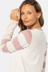 Buzo de tejido fino confeccionado en algodón, con diseño de bloques de color y rayas. Presenta un bloque azul claro en el hombro izquierdo, un bloque beige en el centro y rayas horizontales beige y azul claro en el hombro y brazo derechos. La manga izquierda es de color lila.