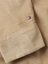 Camisa de manga larga color beige de pana con cuello clásico, cierre frontal con botones, logo de Tommy Hilfiger en la muñeca y detalles distintivos de la marca.