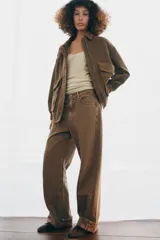Chaqueta oversize confeccionada en piel de ante, con cuello solapa, manga larga con puños elásticos y bajo elástico. Presenta bolsillos de plastrón con solapa en el frente y cierre frontal con cremallera y botones ocultos.