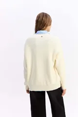 Saco de punto color crema con escote en V, cierre frontal con botones y bolsillos delanteros. Presenta un diseño de calce relajado con estructura marcada.