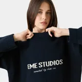 Sweater de punto grueso color azul marino, con cuello redondo, corte cuadrado y ligeramente corto. Presenta gráficos de "EME STUDIOS curated by bien ice" en jacquard blanco en el frente. Tiene puños ajustados.