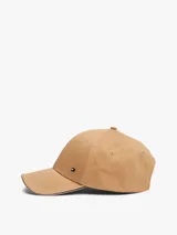 Gorra de béisbol color beige con detalle distintivo de franja tricolor (rojo, blanco y azul) en el borde de la visera. Tiene logo metálico de Tommy Hilfiger en el frente y hebilla metálica ajustable en la parte trasera.