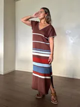 Vestido largo de tejido de punto de algodón, con diseño rayado en tonos marrón, celeste, blanco y rojo. Presenta escote en V con detalle de costura en contraste, mangas cortas, silueta holgada y aberturas laterales en el dobladillo.