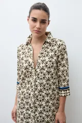 Vestido camisero midi con estampado geométrico en tonos verde oliva y beige. Presenta cuello camisero, cierre frontal con botones, mangas tres cuartos y aberturas laterales en el ruedo.