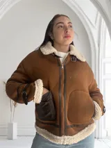 Chaqueta marrón con cuello de piel sintética color crema, cierre frontal con cremallera y hebilla en el cuello, bolsillos laterales con ribete de cuero marrón y puños con ribete de piel sintética.