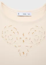 Vestido corto de tejido de punto fino color crema, con cuello barco y sin mangas. Presenta un diseño recto con detalles calados en forma de flores en el pecho y en el ruedo, el cual tiene un acabado festoneado.