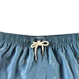 Short de baño color azul con estampado sutil de palmeras, cintura elástica con cordón ajustable, dos bolsillos laterales y un bolsillo trasero con solapa. Cuenta con aberturas laterales en el ruedo.