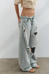 Jeans de tiro medio con corte baggy y diseño de cinco bolsillos. Presenta roturas localizadas en las piernas y cierre frontal con cremallera y botón metálico.