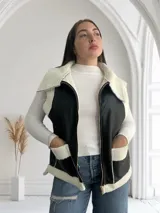 Chaleco negro de ecocuero con interior de corderito blanco, cierre frontal con cremallera y bolsillos laterales.