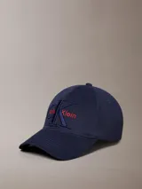 Gorra de béisbol azul marino con visera curva y parte trasera ajustable. Presenta el logo de Calvin Klein bordado en el frente con el monograma CK en azul oscuro y el nombre de la marca en rojo.