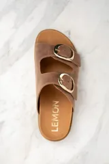 Sandalias marrones de cuero con dos tiras anchas ajustables con hebillas doradas. La plantilla es de corcho y la suela es de goma.