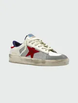 Zapatillas Golden Goose modelo Stardan con diseño tricolor. Presentan cuerpo de cuero blanco con paneles laterales de malla gris, estrella lateral de gamuza roja, puntera de gamuza gris y detalles en azul marino en el talón. Incluyen suela con efecto desgastado característico de la marca.