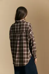 Camisa de estilo leñador con estampado de cuadros en tonos azul, negro y marrón. Presenta cuello clásico, cierre frontal con botones y mangas largas con puños abotonados.