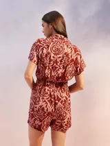 Mono corto negro con estampado floral en tonos beige y amarillo. Presenta cuello camisero, manga corta y un lazo ajustable en la cintura.