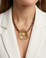 Collar con cordón de efecto carey animal print y dije central de acero bañado en oro con diseño de flor calada y perla en el centro.