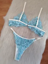 Conjunto de lencería compuesto por un corpiño triangular y una bombacha, confeccionados en encaje floral color aguamarina con detalles de ribetes en color champagne. El corpiño cuenta con breteles regulables y la bombacha presenta laterales ajustables.