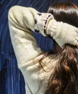 Sweater tejido en lana merino color crudo, con diseño artesanal en jacquard y bordados a mano de figuras geométricas en tonos marrón y terracota. Presenta cuello redondo, mangas largas y silueta relajada.